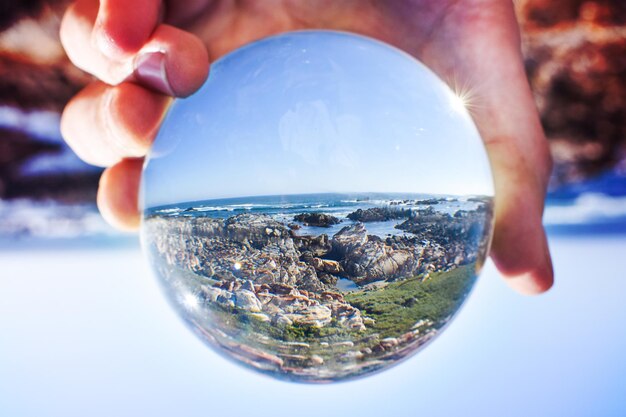 Foto nahaufnahme einer hand, die eine kristallkugel gegen meer und himmel hält