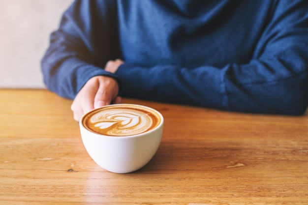 Nahaufnahme einer Hand, die eine Tasse heißen Kaffee auf einem Holztisch hält