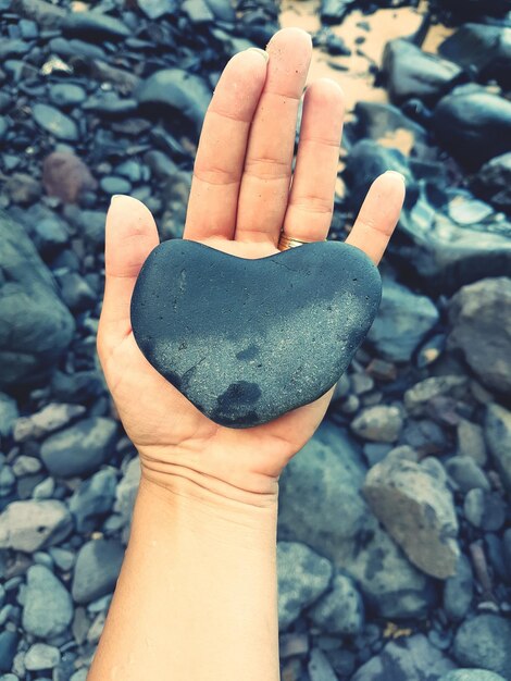 Foto nahaufnahme einer hand, die einen herzförmigen stein am strand hält