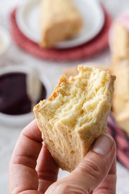 Nahaufnahme einer Hand, die einen Käse-Scones hält. Tisch für den Nachmittagstee mit Käse-Scones