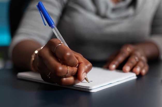 Nahaufnahme einer Hand, die einen Stift hält, um auf eine Lehrbuchdatei zu schreiben und von zu Hause aus an einem Geschäftsprojekt zu arbeiten. Person, die ein Notizbuch verwendet, um Notizen zu machen und Informationen auf Papier zu schreiben. Fernarbeit am Schreibtisch