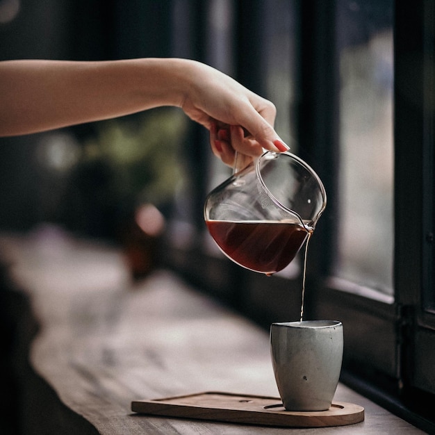 Nahaufnahme einer Hand, die Kaffee in eine Tasse gießt
