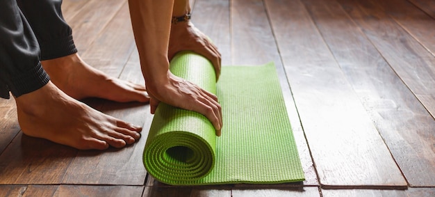 Nahaufnahme einer Hand, die nach dem morgendlichen Training eine grüne Yogamatte oder Trainingsmatte rollt