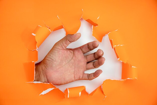 Foto nahaufnahme einer hand, die papier vor orangefarbenem hintergrund hält