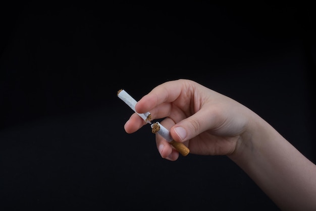 Foto nahaufnahme einer hand, die zerbrochene zigaretten vor schwarzem hintergrund hält