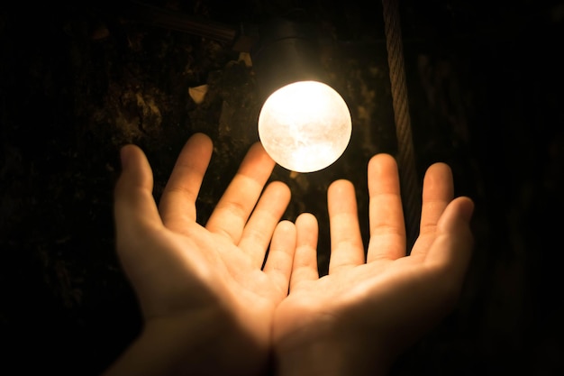 Foto nahaufnahme einer hand mit einer beleuchteten glühbirne vor schwarzem hintergrund