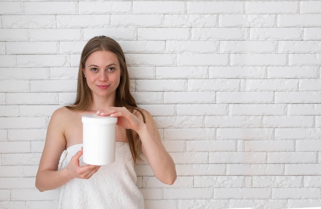 Nahaufnahme einer hübschen langhaarigen kaukasischen Frau, die in ein Handtuch gewickelt ist und ein Glas mit Wachs zur Haarentfernung hält. Schönheitskonzept, Kuranwendungen, Kosmetik. Platz für Text, Platz kopieren