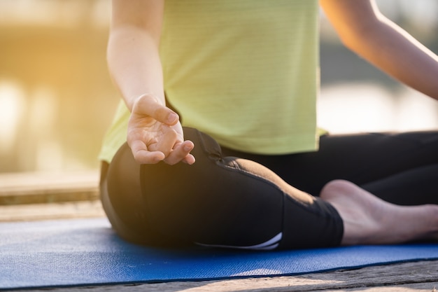 Nahaufnahme einer jungen asiatischen schönen Frau, die Yoga praktiziert und morgens im Lotussitz im Freien neben dem See meditiert, um sich zu entspannen und zu beruhigen. Harmonie- und Meditationskonzept.