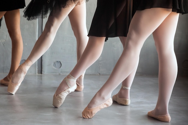 Nahaufnahme einer jungen Balletttänzerin in schwarzen Kleidern, weißen Strumpfhosen und Spitzenschuhen, die eine Socke ziehen