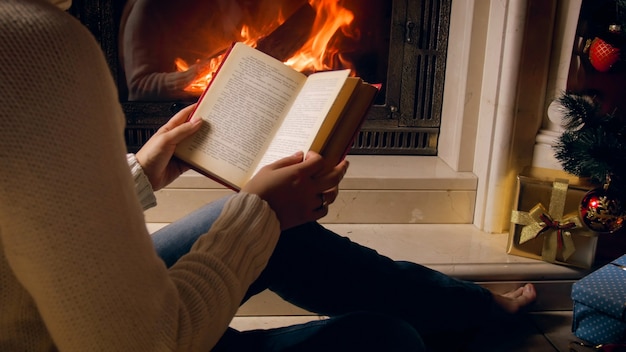 Nahaufnahme einer jungen Frau, die am Kamin sitzt und zu Weihnachten ein Buch liest