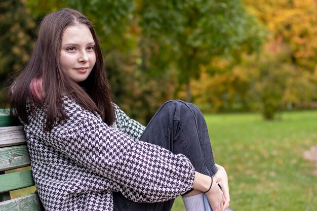 Nahaufnahme einer jungen Frau, die auf einer Bank in einem Herbstpark sitzt