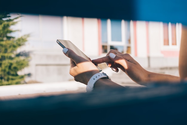 Nahaufnahme einer jungen Frau, die auf einer Bank sitzt und einen Handy genießt