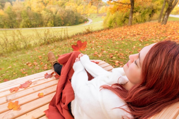 Nahaufnahme einer jungen Frau, die auf einer mit einer orangefarbenen Decke bedeckten Bank sitzt. Frau genießt einen wunderschönen Herbsttag im Park