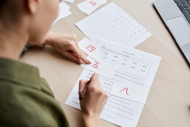 Nahaufnahme einer jungen Frau, die auf Hieroglyphe in einer auf Papier gedruckten Tabelle zeigt, während sie chinesische Langu studiert