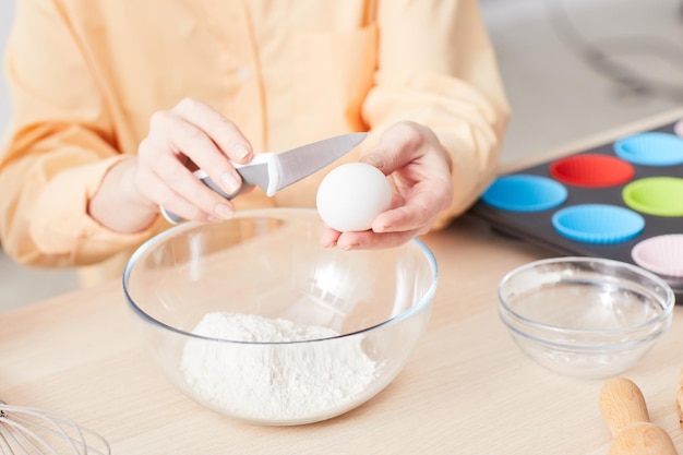 Nahaufnahme einer jungen Frau, die Eier bricht, während sie hausgemachte Muffins im Küchenkopierraum backt