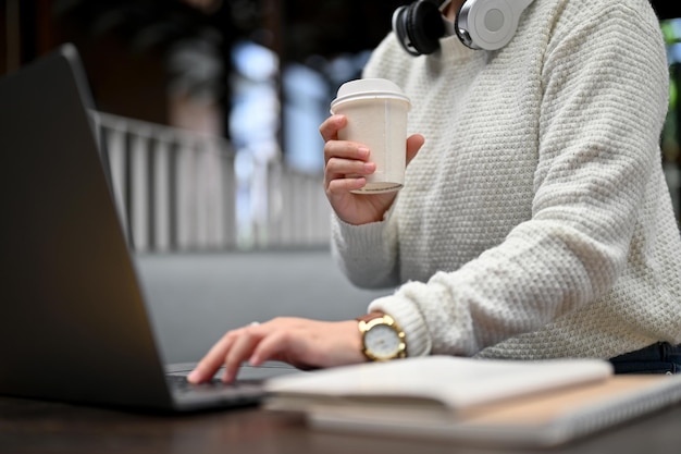 Nahaufnahme einer jungen Frau, die in einem Café arbeitet, Laptop tippt und Kaffee trinkt