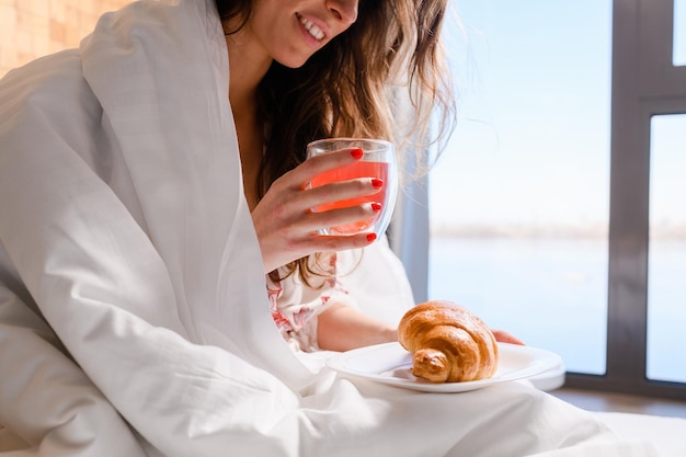 Nahaufnahme einer jungen Frau, die morgens im Bett frühstückt