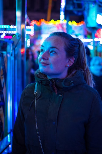 Nahaufnahme einer jungen Frau, die nachts vor einem beleuchteten Vergnügungspark steht