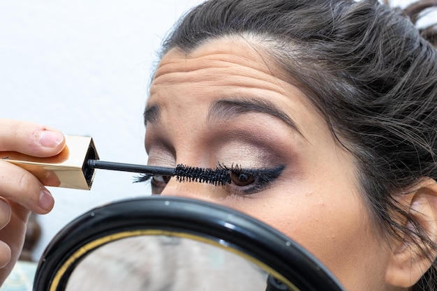 Nahaufnahme einer jungen Frau, die Wimperntusche mit einem Handspiegel aufträgt