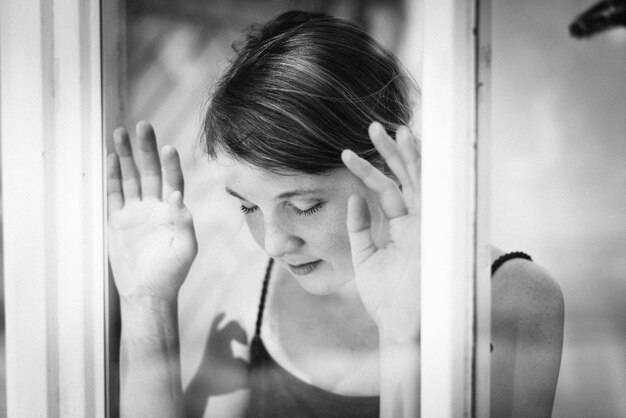 Nahaufnahme einer jungen Frau mit der Hand auf dem Fenster