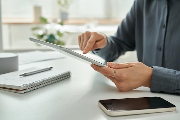 Nahaufnahme einer jungen Geschäftsfrau, die Tablet-PC verwendet und online arbeitet, während sie am Tisch im Büro sitzt