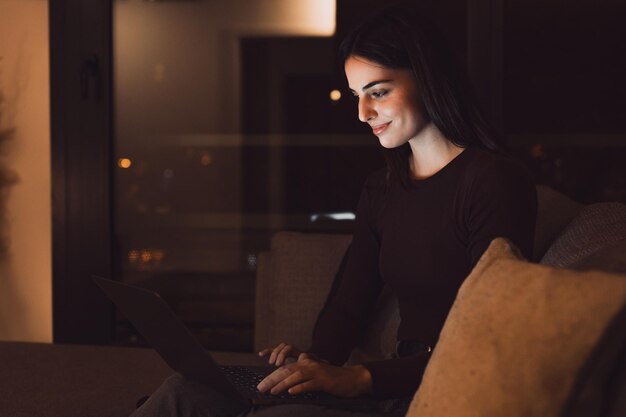 Nahaufnahme einer jungen, glücklichen, fröhlichen Frau, die lächelt und zu Hause auf dem Sofa sitzt und einen Laptop benutzt