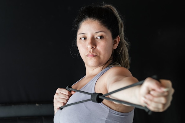 Nahaufnahme einer jungen Latina-Frau, die mit ihren Händen ein Gummiband dehnt, um ihre Muskeln zu trainieren