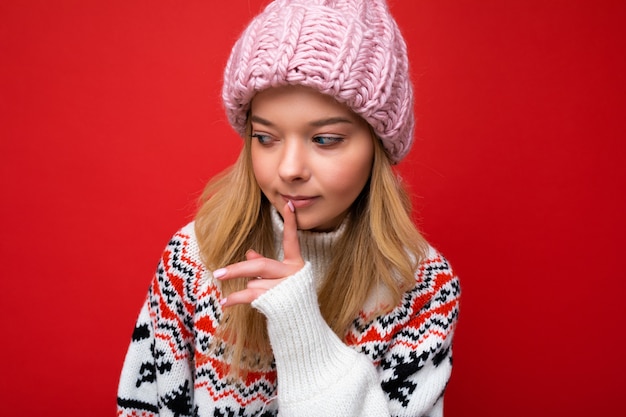 Nahaufnahme einer jungen schönen blonden Frau mit aufrichtigen Emotionen, die rosa Hut und Winterpullover trägt