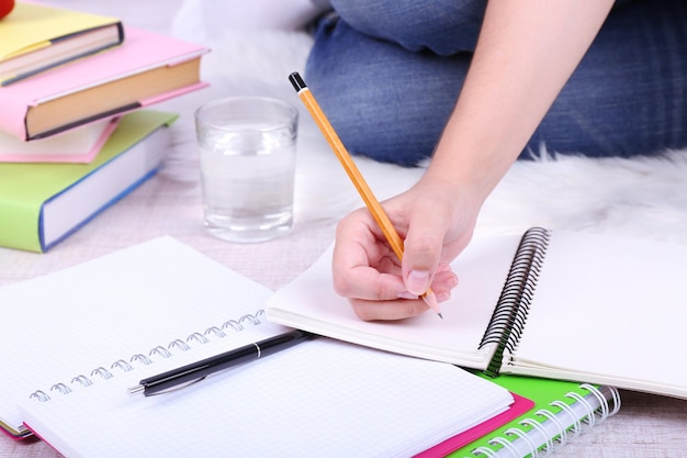 Nahaufnahme einer jungen Studentin, die auf dem Boden sitzt und auf hellem Hintergrund studiert