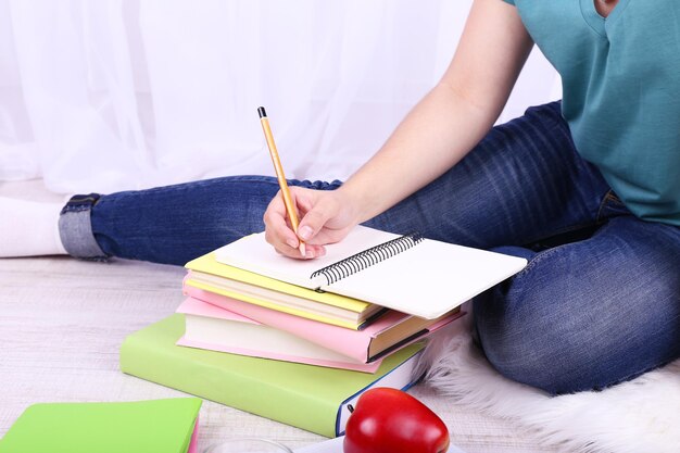 Nahaufnahme einer jungen Studentin, die auf dem Boden sitzt und auf hellem Hintergrund studiert