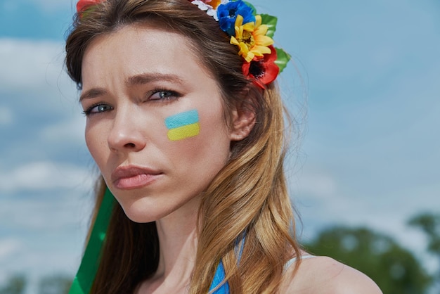 Nahaufnahme einer jungen ukrainischen frau in blumenkrone, die mit himmel im hintergrund in die kamera blickt