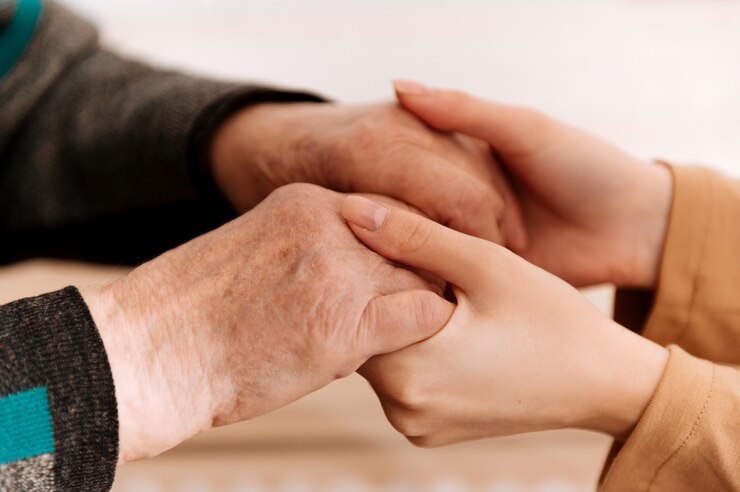 Nahaufnahme einer jungen weiblichen Hand, die die älteren Hände einer alten Frau tröstet