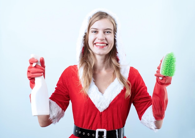 Nahaufnahme einer kaukasischen glücklichen Frau, die Weihnachtsmannkleidung trägt und Handschuhe hält, die Reinigungsspray und -bürste halten