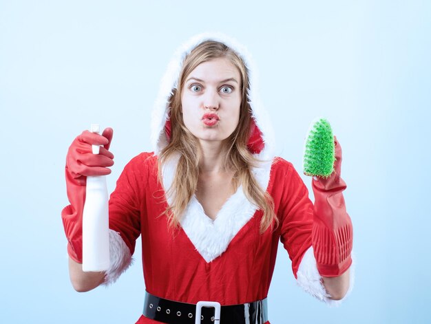 Nahaufnahme einer kaukasischen glücklichen Frau, die Weihnachtsmannkleidung trägt und Handschuhe hält, die Reinigungsspray und -bürste halten