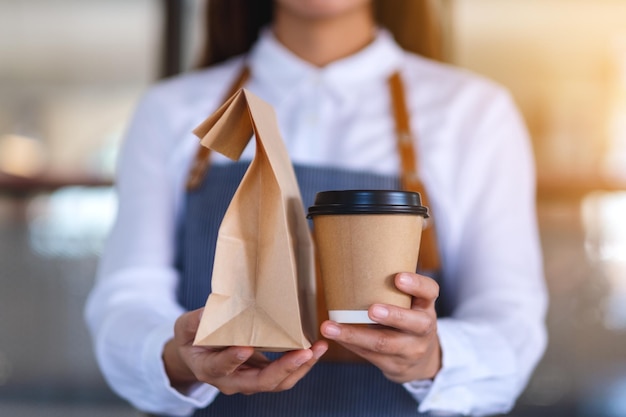 Nahaufnahme einer Kellnerin, die dem Kunden in einem Geschäft eine Papptasse Kaffee und Speisen zum Mitnehmen in einer Papiertüte hält und serviert