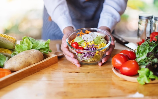 Nahaufnahme einer Köchin, die eine Schüssel mit frischem gemischtem Gemüsesalat in der Küche kocht und hält