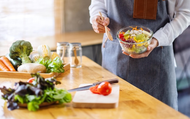 Nahaufnahme einer Köchin, die eine Schüssel mit frischem gemischtem Gemüsesalat kocht und hält, um in der Küche zu essen