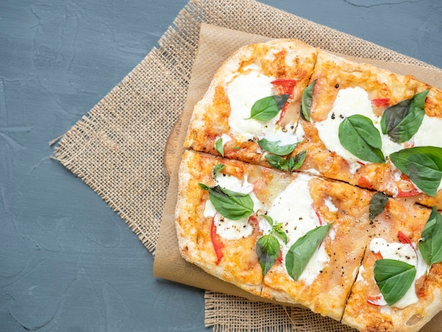 Nahaufnahme einer köstlichen, frischen, knusprigen römischen Pizza mit Käse und Kräutern auf grauem Hintergrund Bastelpapier-Leinenserviette Draufsicht flach liegend