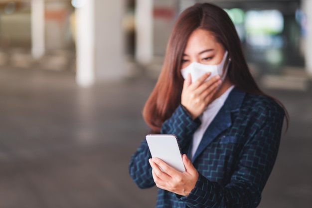 Nahaufnahme einer kranken Frau, die eine schützende Gesichtsmaske trägt und ein Mobiltelefon für das Gesundheitswesen und das Covid-19-Konzept verwendet