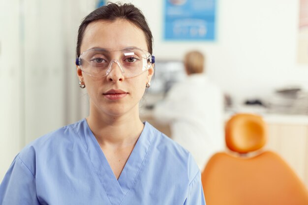 Nahaufnahme einer Krankenschwester in Uniform, die in die Kamera schaut, während sie im Büro des Stomatologie-Krankenhauses arbeitet