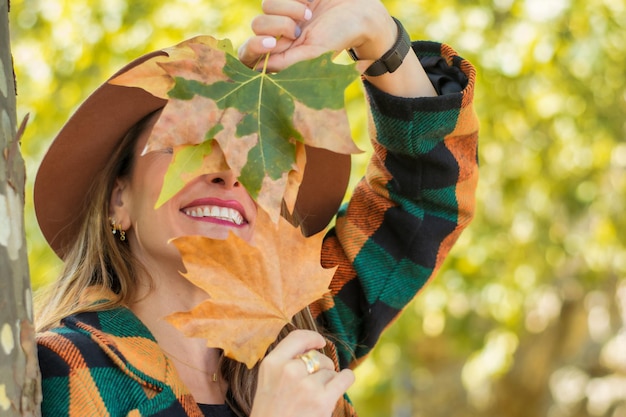 Nahaufnahme einer lächelnden Frau mit Herbstlaub auf ihrem Gesicht.