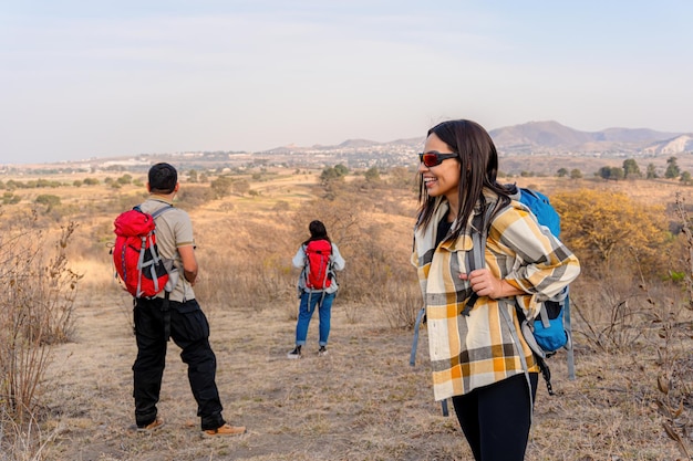 Foto nahaufnahme einer lächelnden lateinamerikanischen frau, die einen bergweg entlang geht. um sie herum genießen andere wanderer die natur und die natur, was ein gefühl der gemeinschaft und des gemeinsamen abenteuers schafft.