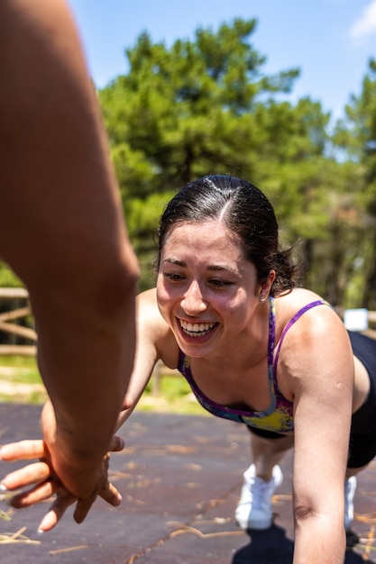 Nahaufnahme einer lächelnden lateinamerikanischen Frau, die mit ihrem Trainingspartner in einem Sportpark im Freien Plankenübungen macht