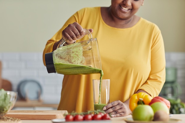 Nahaufnahme einer lächelnden schwarzen Frau, die zu Hause einen gesunden Smoothie in der Küche genießt