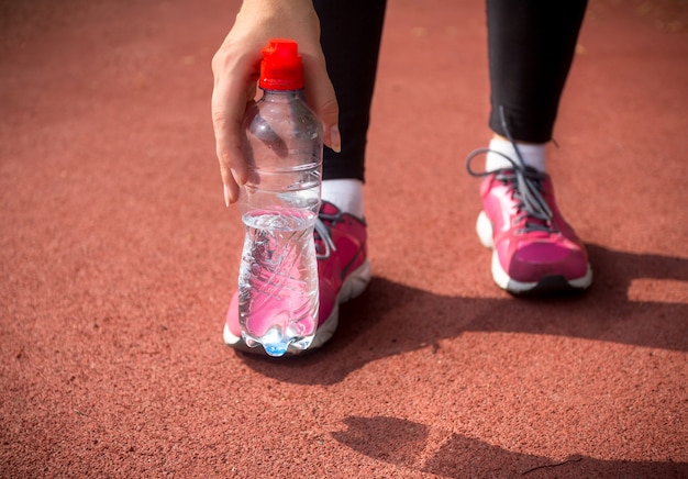 Nahaufnahme einer Läuferin, die eine Plastikflasche Wasser auf der Laufstrecke hält