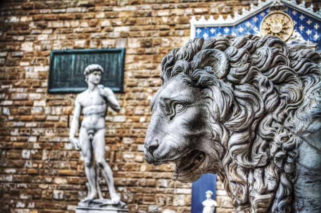 Nahaufnahme einer Löwenkopfstatue in Lanzi della Loggia mit Michelangelos David im Hintergrund in Florenz, Italien