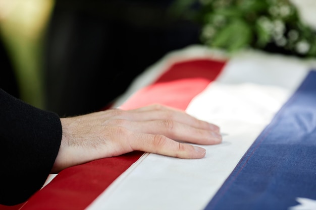 Nahaufnahme einer männlichen Hand auf einem Sarg mit amerikanischer Flagge bei einer Trauerzeremonie im Freien für eine Armeeveteranenkopie