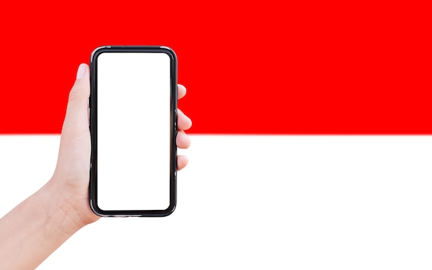 Nahaufnahme einer männlichen Hand, die ein Smartphone mit leerem Bildschirm auf dem Hintergrund der unscharfen Flagge Indonesiens hält