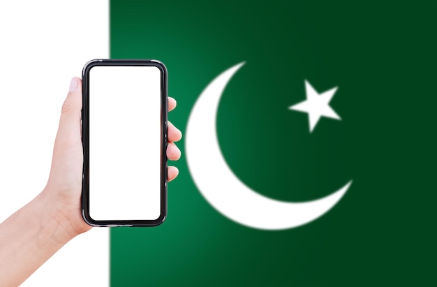 Nahaufnahme einer männlichen Hand, die ein Smartphone mit leerem Bildschirm auf dem Hintergrund der unscharfen Flagge Pakistans hält