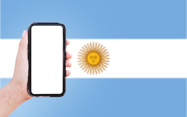 Nahaufnahme einer männlichen Hand, die ein Smartphone mit Leerzeichen auf dem Bildschirm auf dem Hintergrund der unscharfen Flagge Argentiniens hält